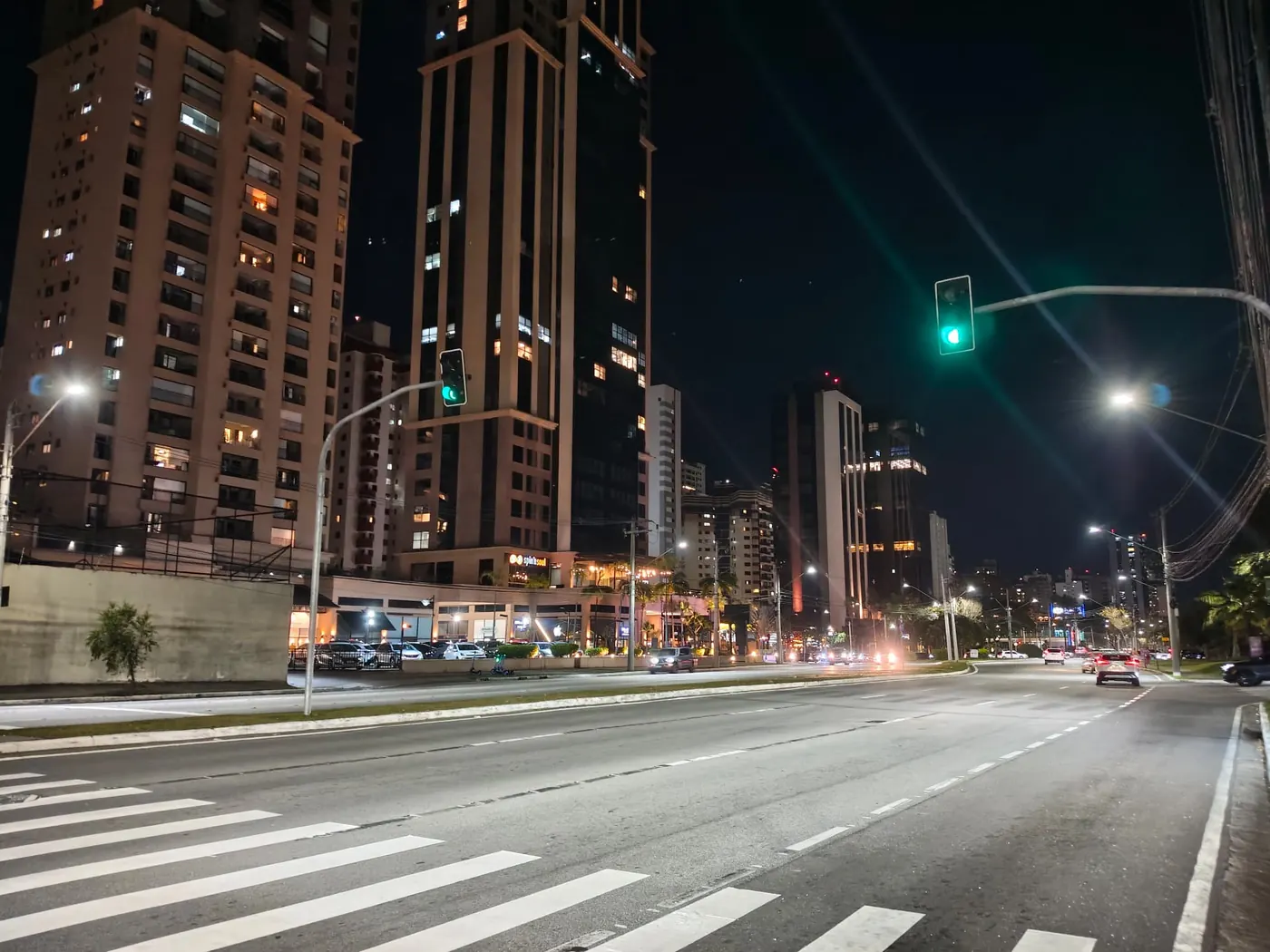 Avenida do Jardim Aquarius à noite, com torres residenciais e comércio iluminado